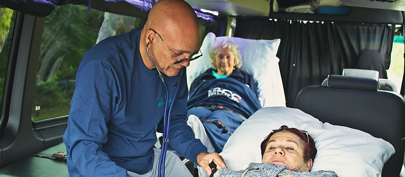 ACC Medlink medical attendant caring for two patients in beds inside a transport van